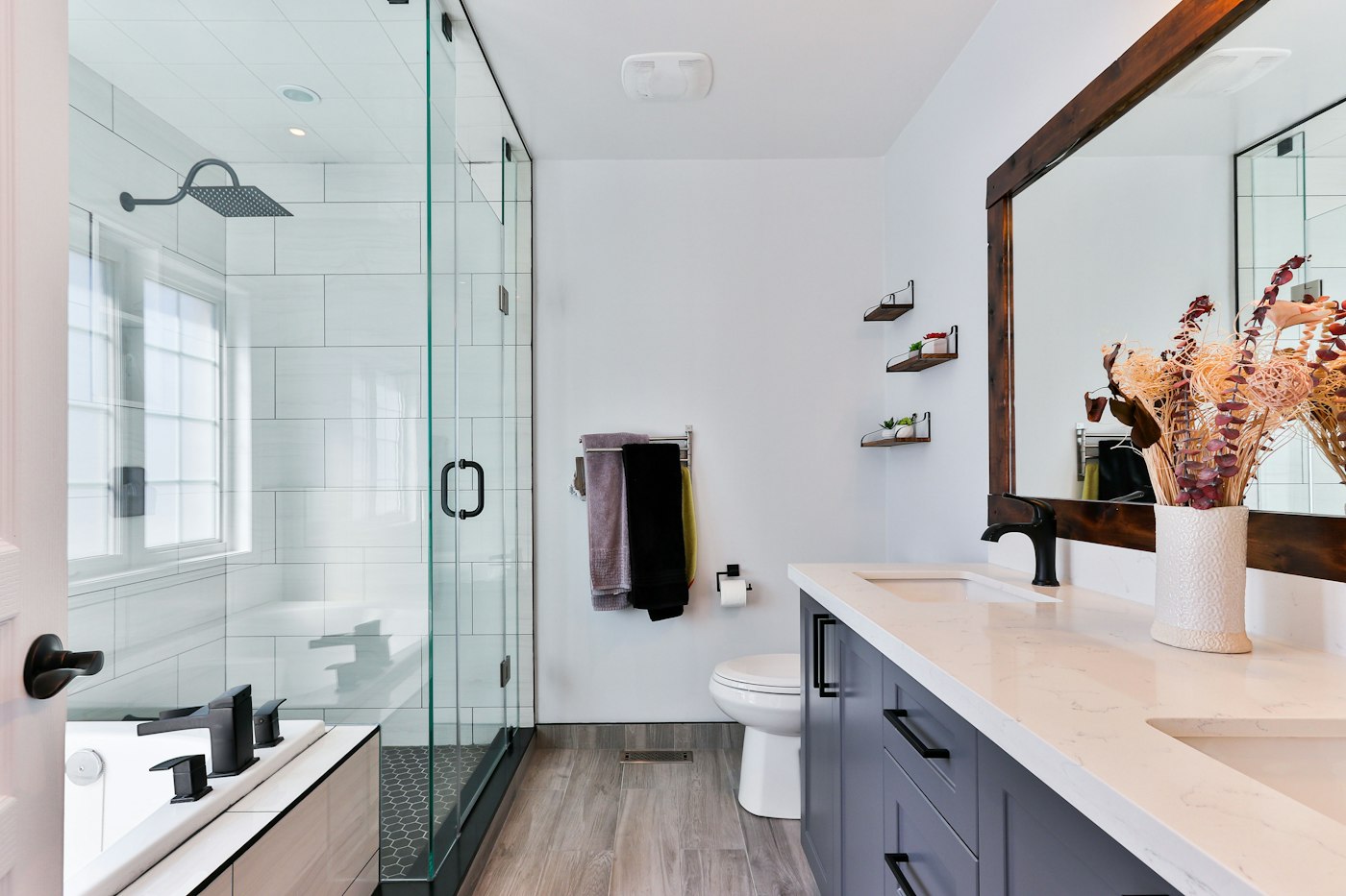 A bathroom with a glass shower enclosure, white wall tiles, and a dark vanity