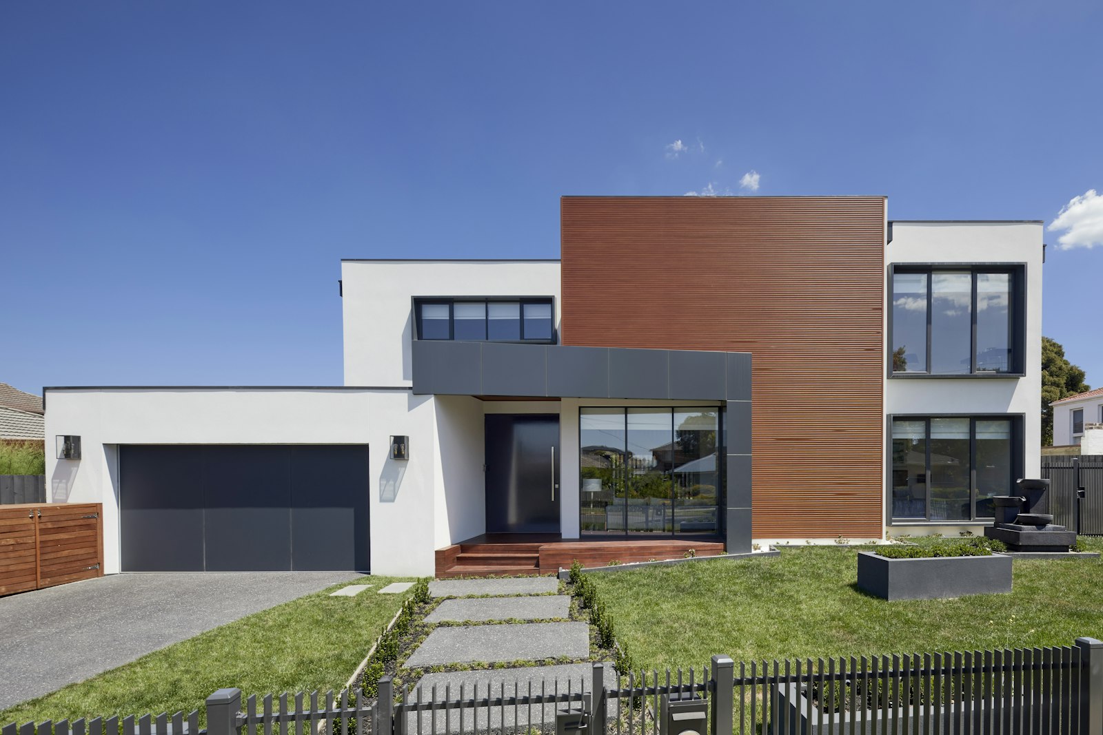 A modern two-storey house with white rendered walls, timber cladding, a garage, and a front lawn
