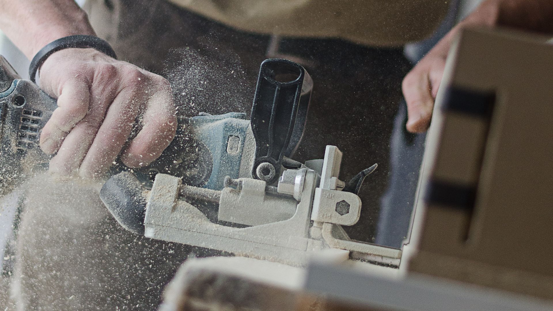 Hands guiding a biscuit joiner through a piece of timber, with sawdust in the air