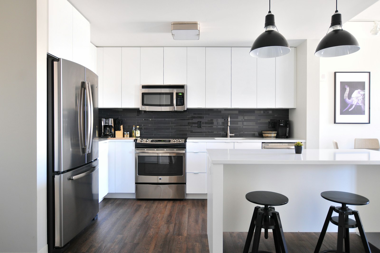 A white kitchen with a stainless steel cooker, a dark tiled splashback, and a central island